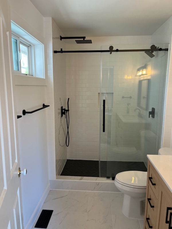 A finished bathroom with a black-framed glass shower and white subway tile, plumbed by Ports Plumbing