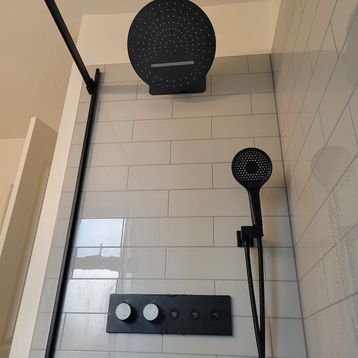 Matte-black rainfall shower head and thermostatic controls on white subway tile