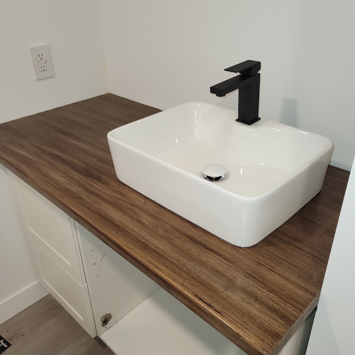 White vessel basin with a square matte-black faucet on a butcher-block vanity