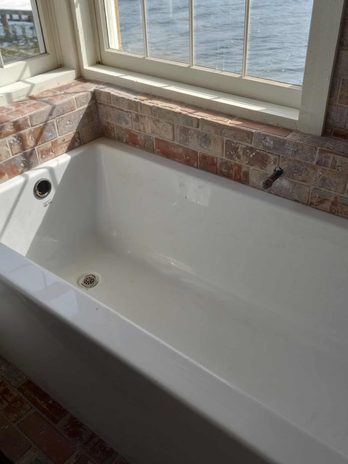 Freestanding soaker tub set into a reclaimed-brick surround with a lakeside window